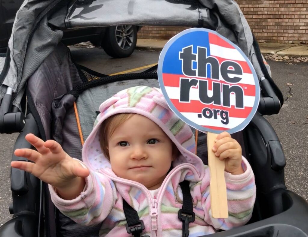 A baby in stroller holding up a sign that says " the run."